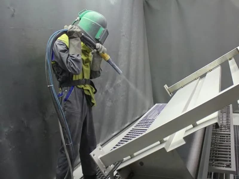 Technician in protective suit applying protective primer coating using spray gun